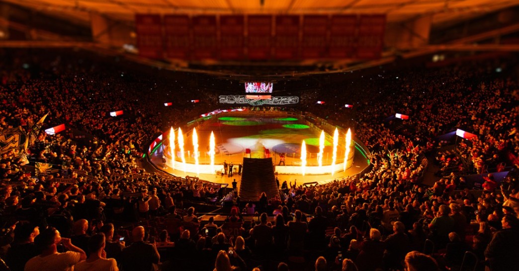 En nedsläkt ishockeyarena med massa publik och eldpelare på isen i mitten