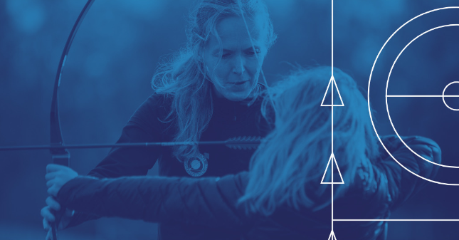 En kvinnlig tränare instruerar en ung bågskytt hur hon ska spänna bågen.